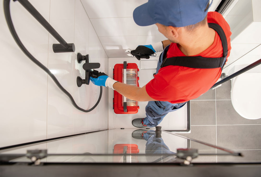a person in a blue hat and gloves holding a tool box on a shower room